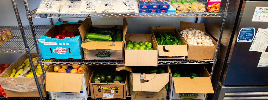 3 of 5, Shelf of fresh produce including boxes of red tomatoes, green zucchinis, green limes, green jalapeños, and white mushrooms.